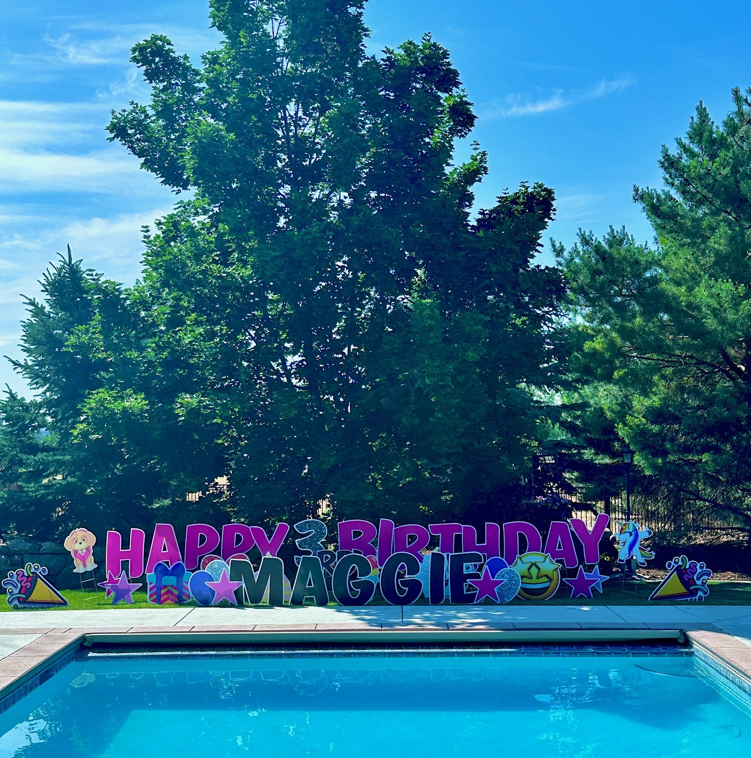 Happy 2nd Birthday Maggie yard card display with purple mermaid letters and birthday art beside a sparkling Boise pool